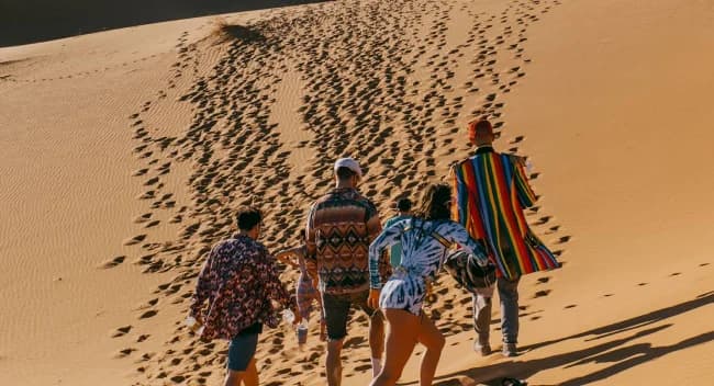 A group of people walk through sand dunes